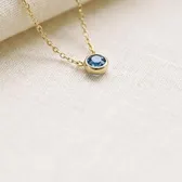 A tiny round blue stone on a fine gold chain, on ivory linen