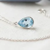 A pale blue pear-shaped topaz pendant on a silver chain, on ivory linen
