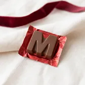 A milk chocolate letter M on red foil, on ivory linen