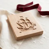 A carved wooden speculaas mold with a sailing ship, on ivory linen