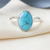 A sterling silver ring with an oval turquoise in a plain bezel, on ivory linen