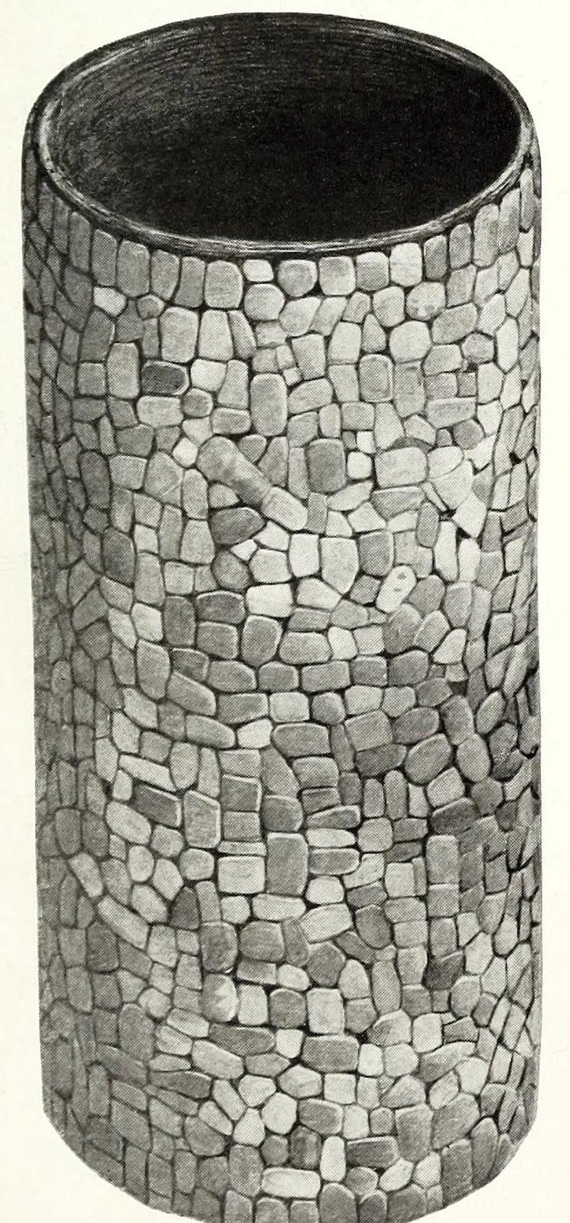 Black-and-white photograph of a tall cylindrical basket covered all over in small fitted pieces of turquoise