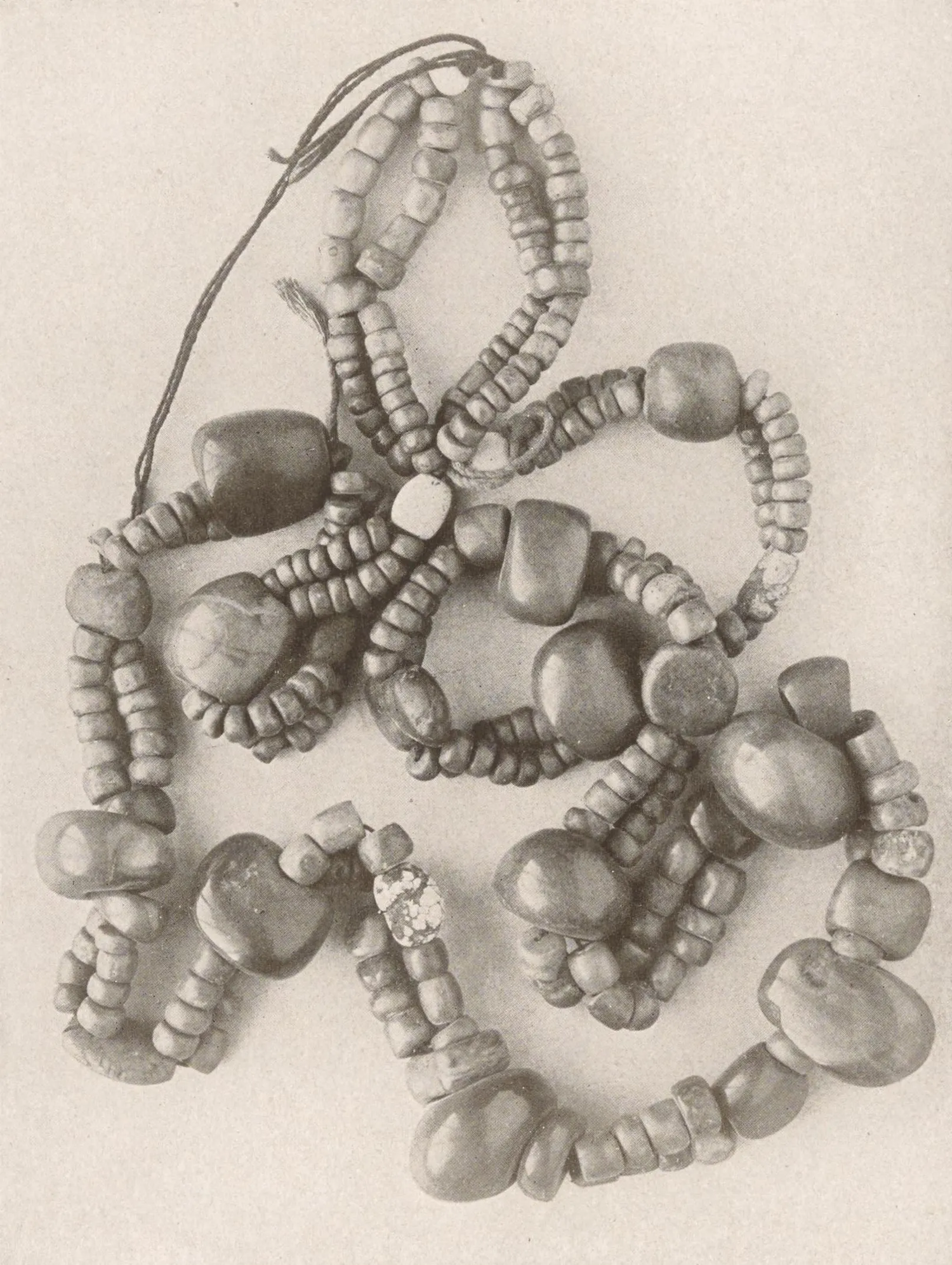 Black-and-white photograph of a Tibetan necklace: several loose strands of small turquoise beads strung with larger rounded turquoise stones